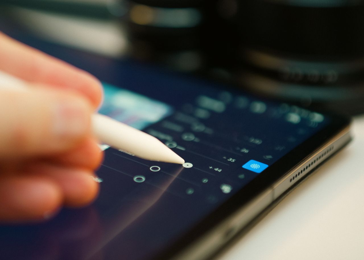 Close-up of a hand using a stylus on a digital tablet for photo editing.